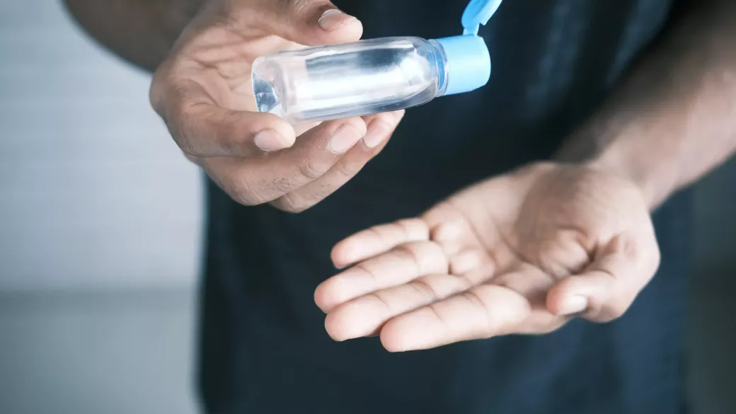 A close up of a person dispensing hand sanitizer from a clear bottle into their palm, emphasizing hygiene and health safety.