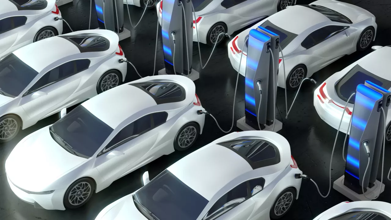 A cluster of modern white electric cars are parked and charging at multiple futuristic charging stations. Each vehicle is connected to a station via charging cables, indicating a focus on clean energy and electric mobility. The scene appears orderly and technologically advanced.