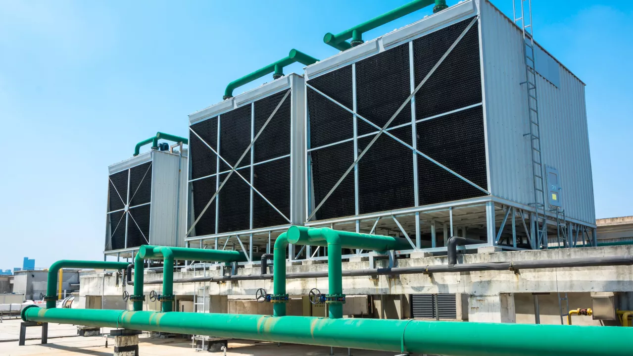 Large industrial air conditioning units on a building rooftop with green piping system under a clear sky.
