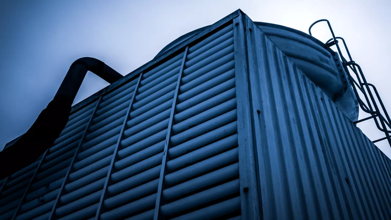 Low angle view of a large industrial air conditioning unit with metal vents and tubing against a moody blue sky.