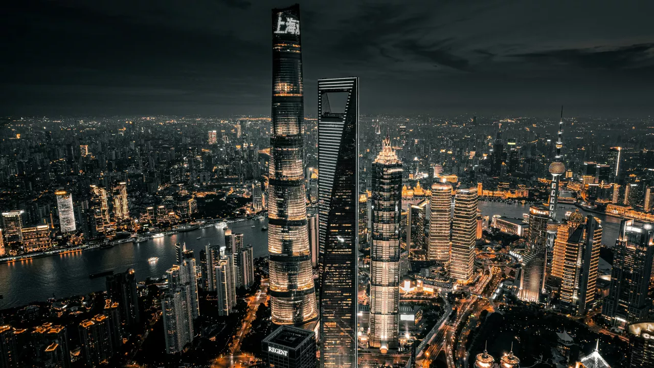 Aerial view of Shanghai at night, showcasing the brightly lit skyline with the prominent Shanghai Tower and surrounding skyscrapers along the Huangpu River.