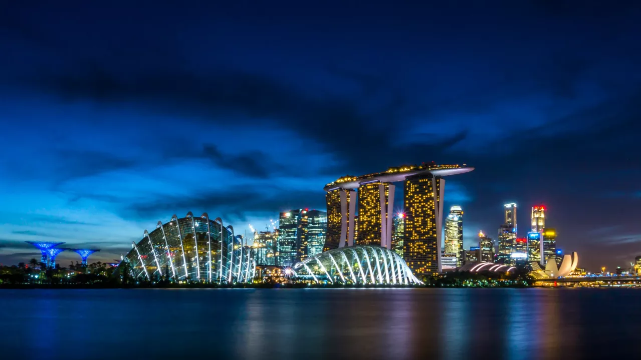 A nighttime view of the Singapore skyline showcasing the Marina Bay Sands, Gardens by the Bay, and Art Science Museum, with vibrant city lights reflected in the water.