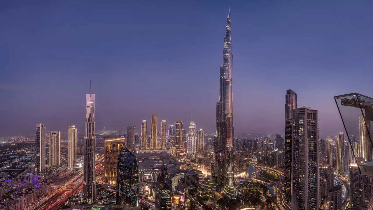 A panoramic view Dubai's skyline at dusk featuring the illuminated Burj Khalifa amidst other skyscrapers and bustling city lights.