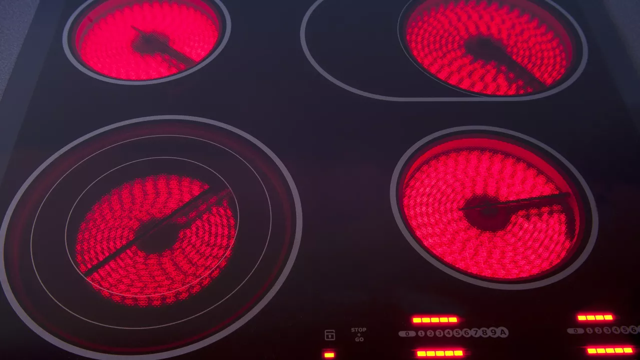 Close-up of a modern electric stove top with four strong radiant ceramic burners, two of which are glowing bright red indicating they are turned on.