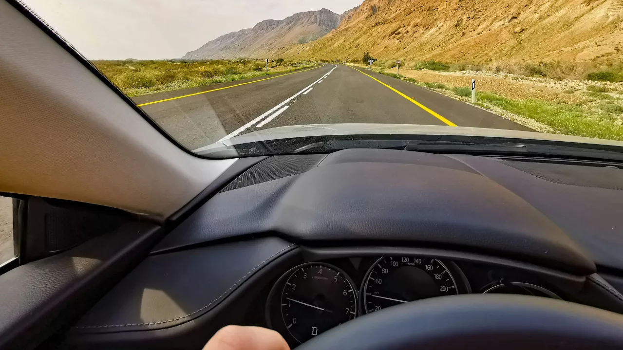 View from a car's driver seat featuring a road stretching through a mountainous landscape.