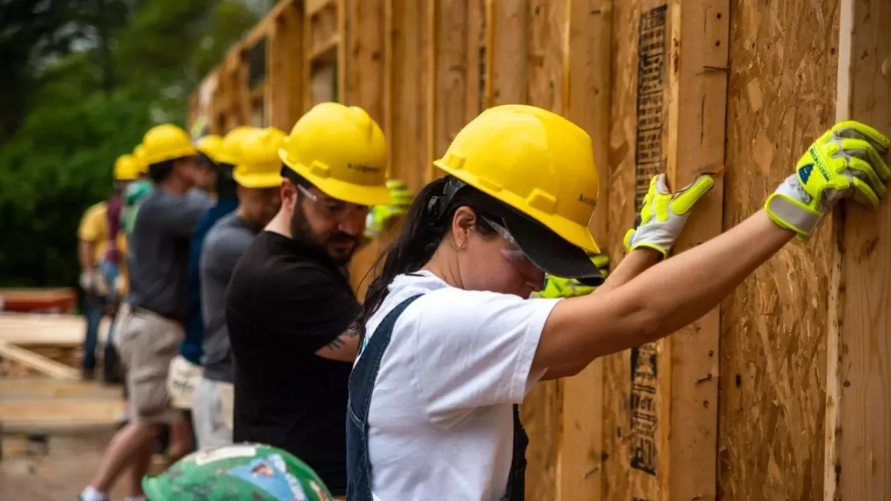A group of construction workers wearing yellow helmets and gloves busy at work, installing wooden panels on a building site.