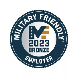 A circular emblem with a dark blue border. The inner part has "Military Friendly Employer" written around the edge and "2023 Bronze" in the center, with a stylized "MF" logo featuring stars and stripes.