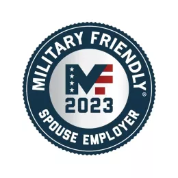 Circular badge with "Military Friendly Spouse Employer" written around the edge. The center features "2023" below a stylized "MF" with stars and stripes design. The badge's border is dark blue, and the text and design elements are white and red.
