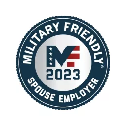 Circular badge with "Military Friendly Spouse Employer" written around the edge. The center features "2023" below a stylized "MF" with stars and stripes design. The badge's border is dark blue, and the text and design elements are white and red.