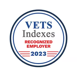 A circular badge features the text "VETS Indexes RECOGNIZED EMPLOYER 2023". "VETS" is in blue, "Indexes" is in gray, "RECOGNIZED EMPLOYER" is in red, and "2023" is in blue below red stripes. The badge is outlined with blue and white borders.