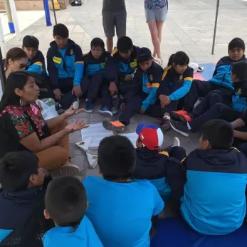 Chilean youth gathered in seated circle around adult facilitator doing an activity