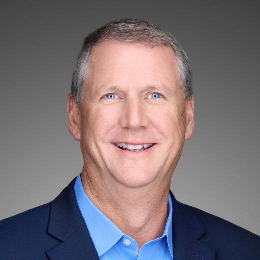 Headshot of Mark Mummert Senior Vice President, Capital Projects and Integrated Supply Chain who has short gray hair, is smiling gently at the camera, and is dressed in a black suit with a blue shirt.