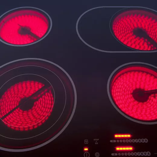 Close-up of a modern electric stove top with four strong radiant ceramic burners, two of which are glowing bright red indicating they are turned on.