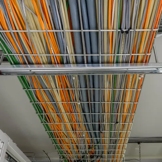 Wire baskets hanging from the ceiling, filled with numerous colored internet cables, viewed from below.