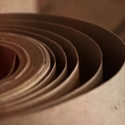 Close-up of stacks of rolled up cardboard with concentric layers, viewed from the side, against a textured beige background.