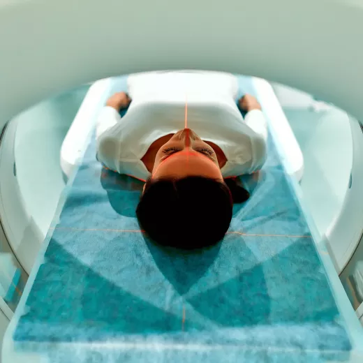 A person lying on their back inside a medical imaging scanner, viewed from above. The focus highlights the centered head and upper body, enveloped in a calm, bright clinical setting.