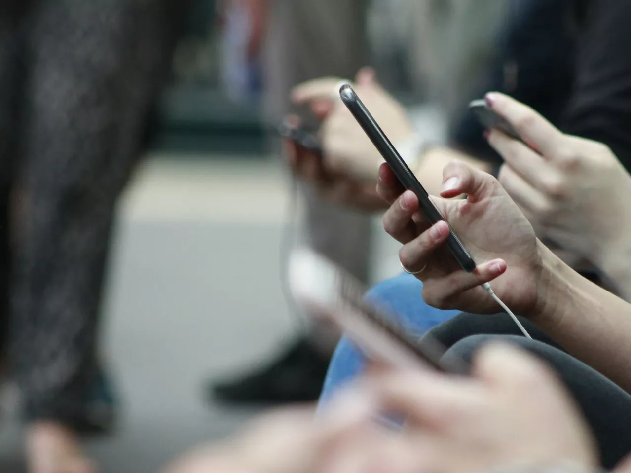 Close-up of a person's hand holding a smartphone connected to earphones, among other commuters, subtly emphasizing modern connectivity and personal space in public.