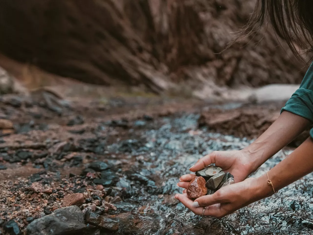 A close-up of a person's hand holding rocks in a clean safe river.
